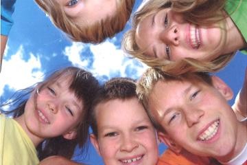 Fünf Kinder stehen im Kreis und schauen nach unten in die Kamera