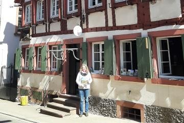 Mitarbeiterin der Touristinfo steht mit Prospekten vor dem Haus