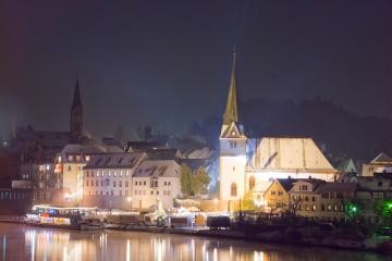 Der Weihnachtsmarkt auf dem Neckarlauer und die Schneebedeckte Kirche spiegeln sich im Fluss