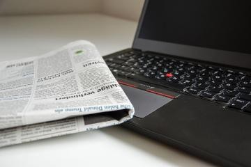 Eine Zeitung liegt schräg auf einem geöffneten Laptop